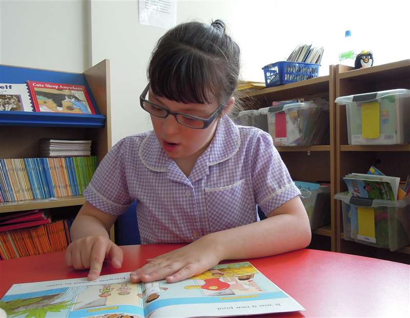 A photograph of a girl with Down syndrome reading a book